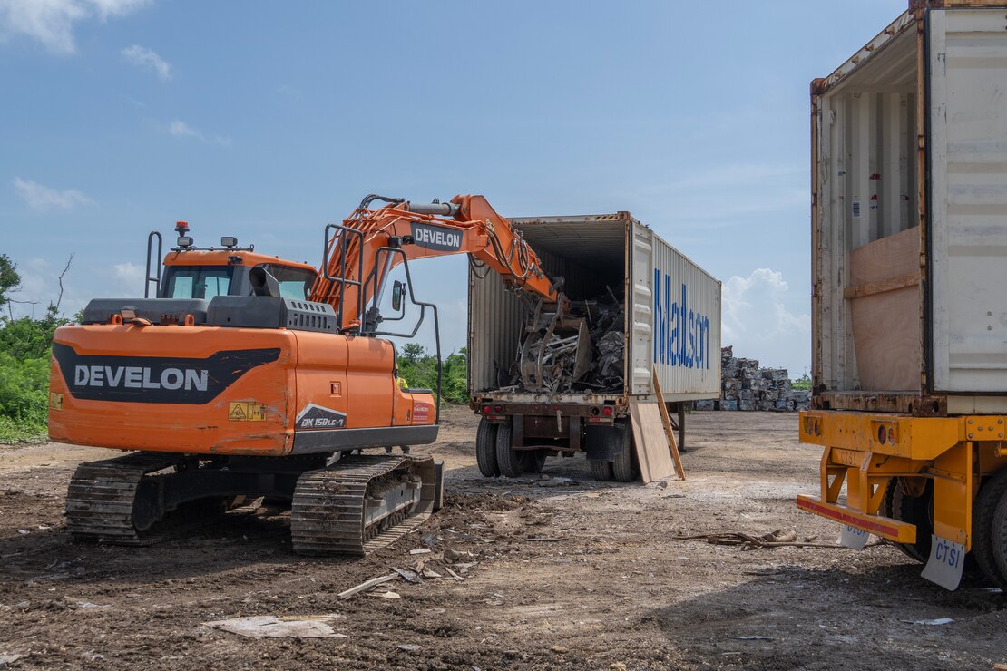 An excavator places a pile of debris into a shipping container.