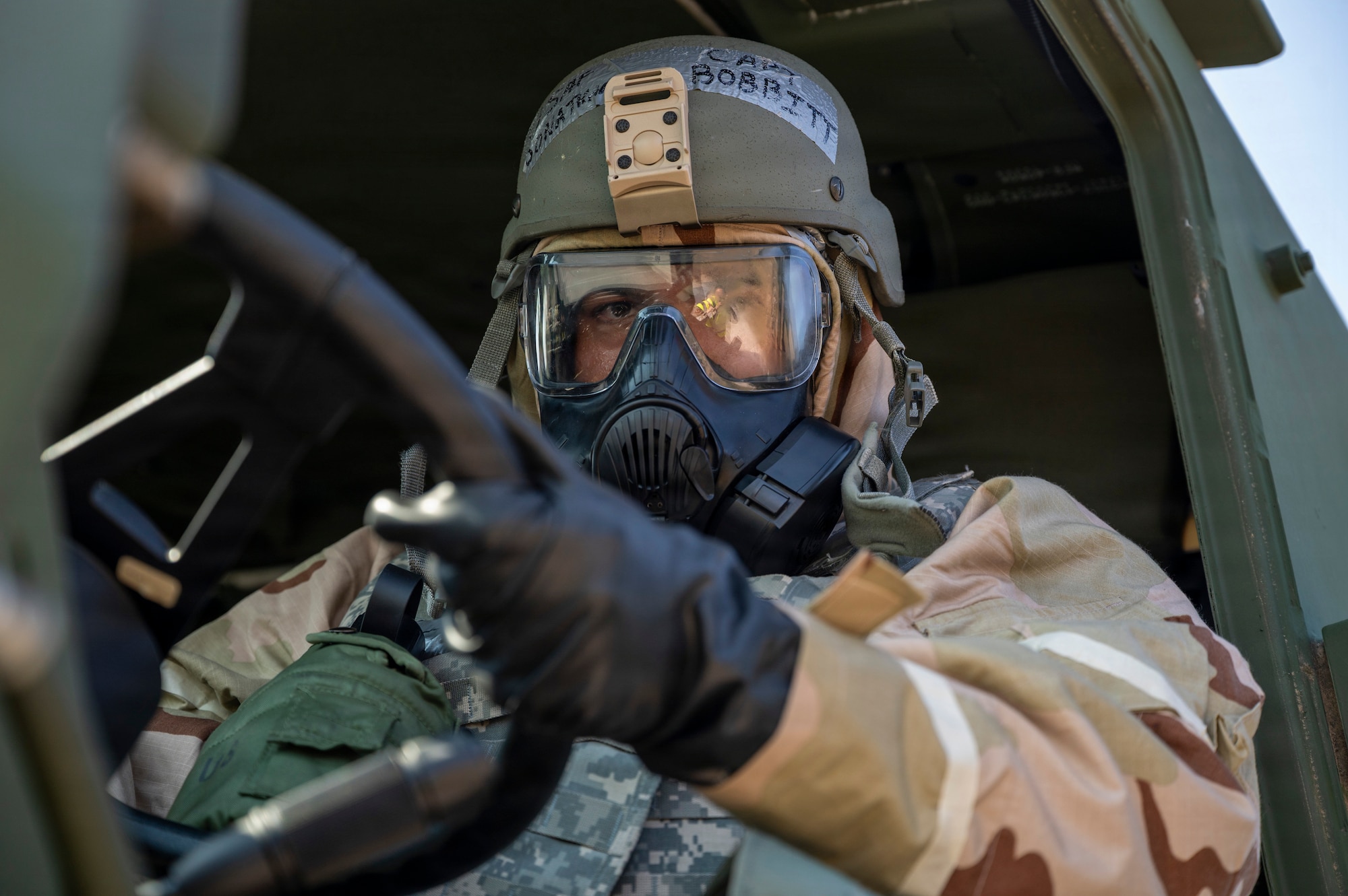 A man drives a truck in MOPP gear.