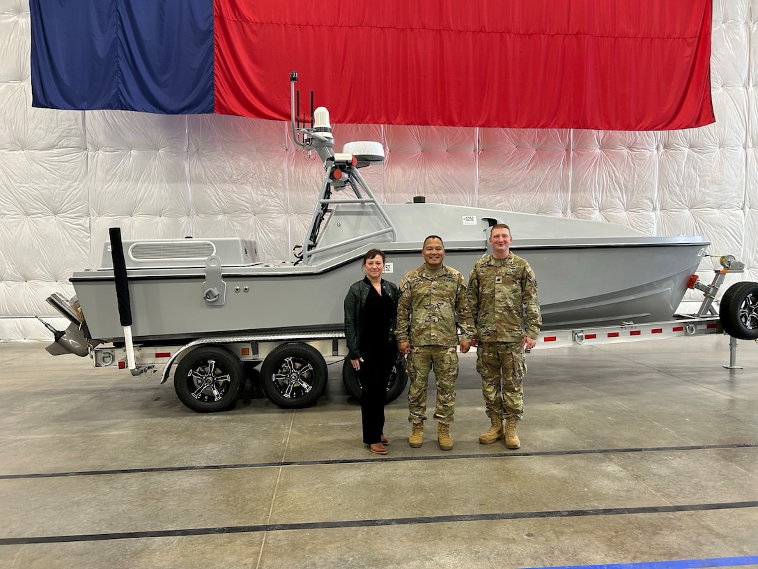 Three people pose for a photo in front of an autonomous surface vessel.
