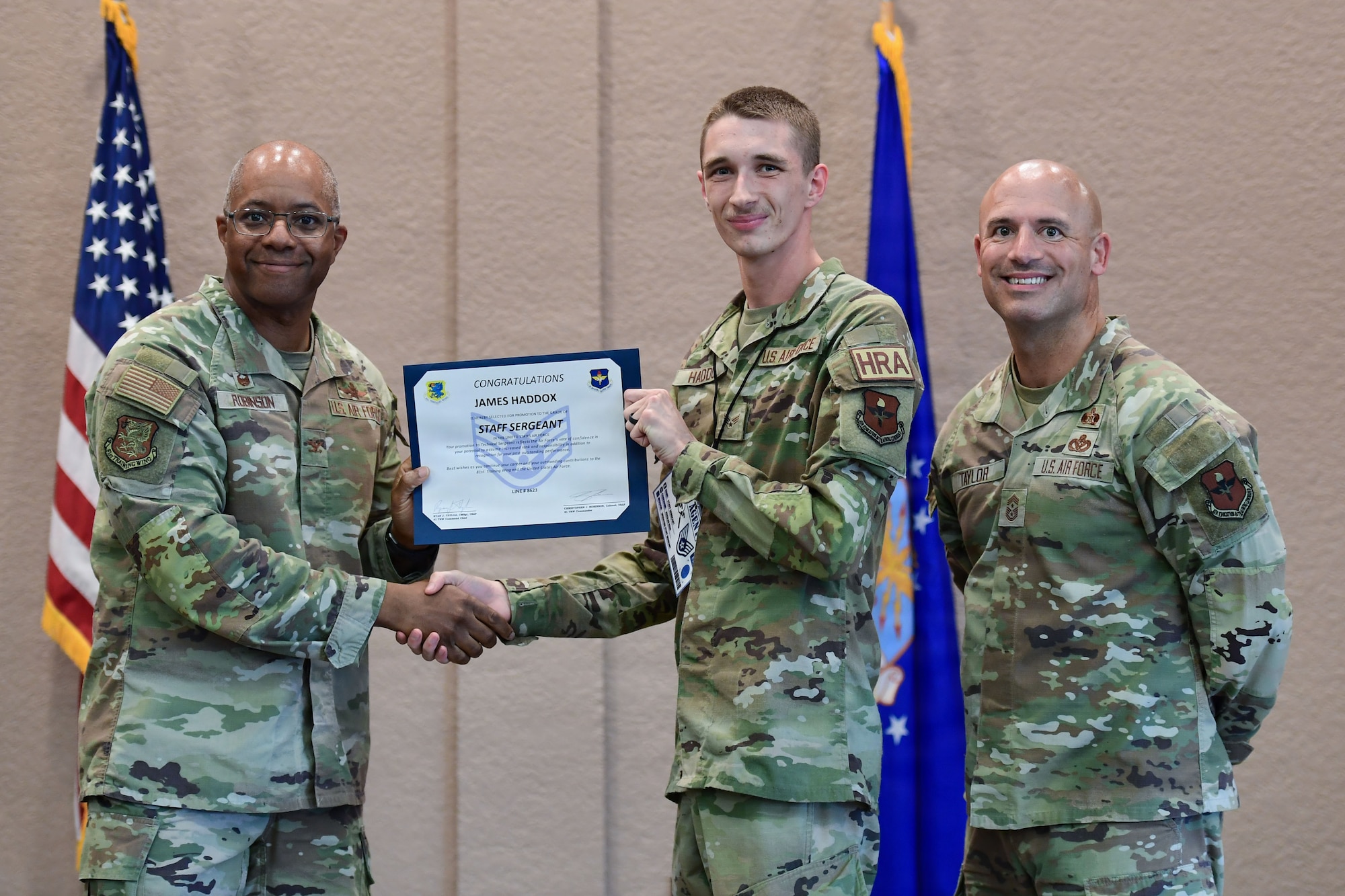Two men in U.S. Air Force uniforms present a certificate to an Airman.