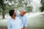 Man and woman in blue shirts smile at each other while standing in a park