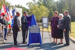 Four people watch as a person unveils a metal plaque at an outside event.
