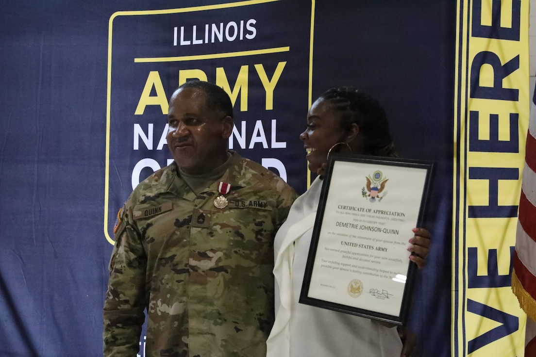 1st Class David Quinn stands alongside his spouse, Demetrie Quinn, as she displays her Certificate of Appreciation during his retirement ceremony