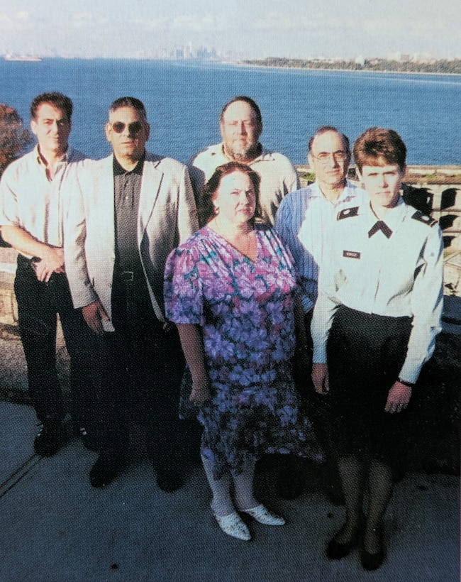 Six people stand outside with the New York City skyline in the background.