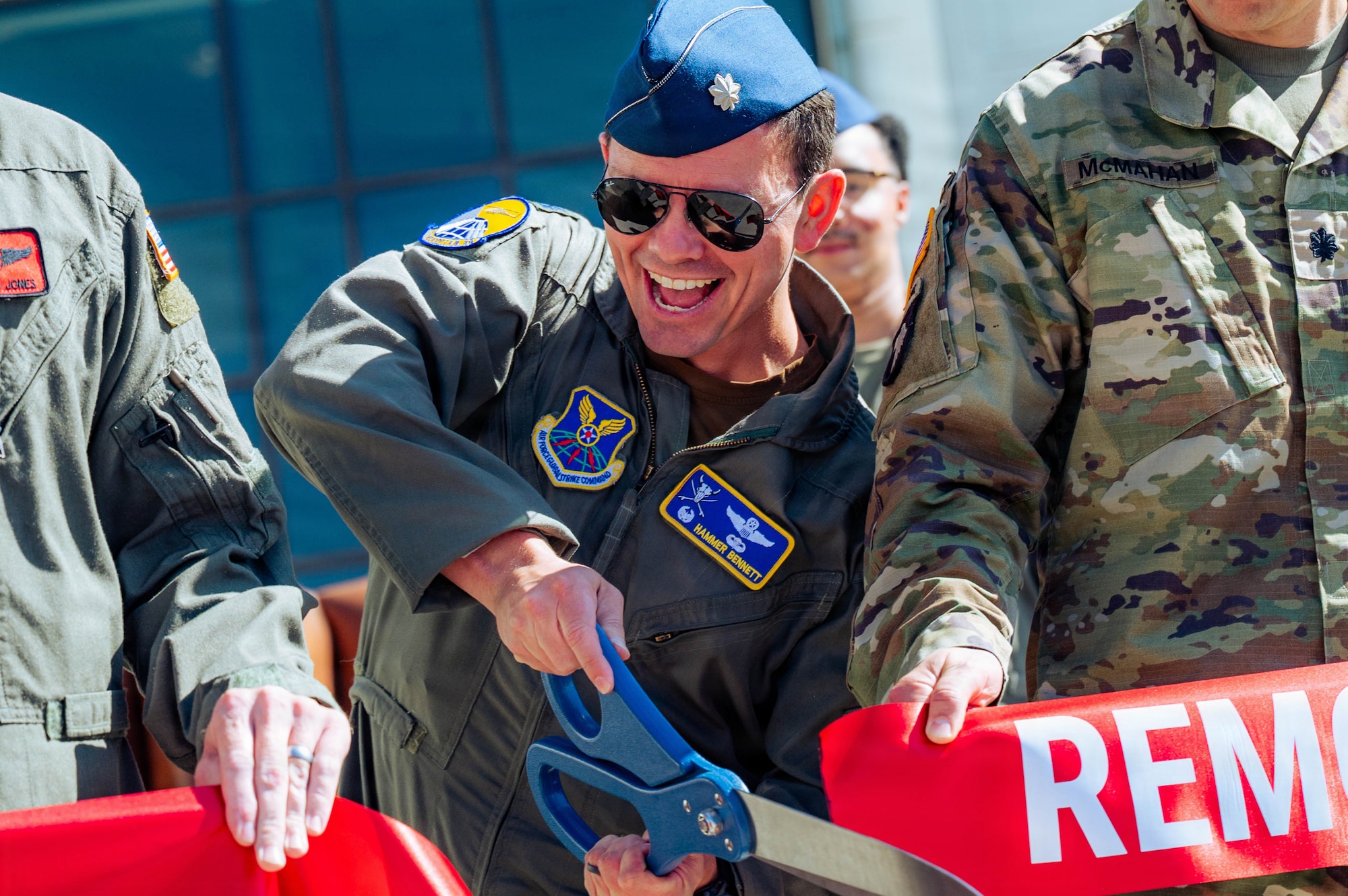 Col. Bennet cuts a ribbon with a large pair of scissors in front of the 37th Helicopter and 90 MSOS TRF Building.