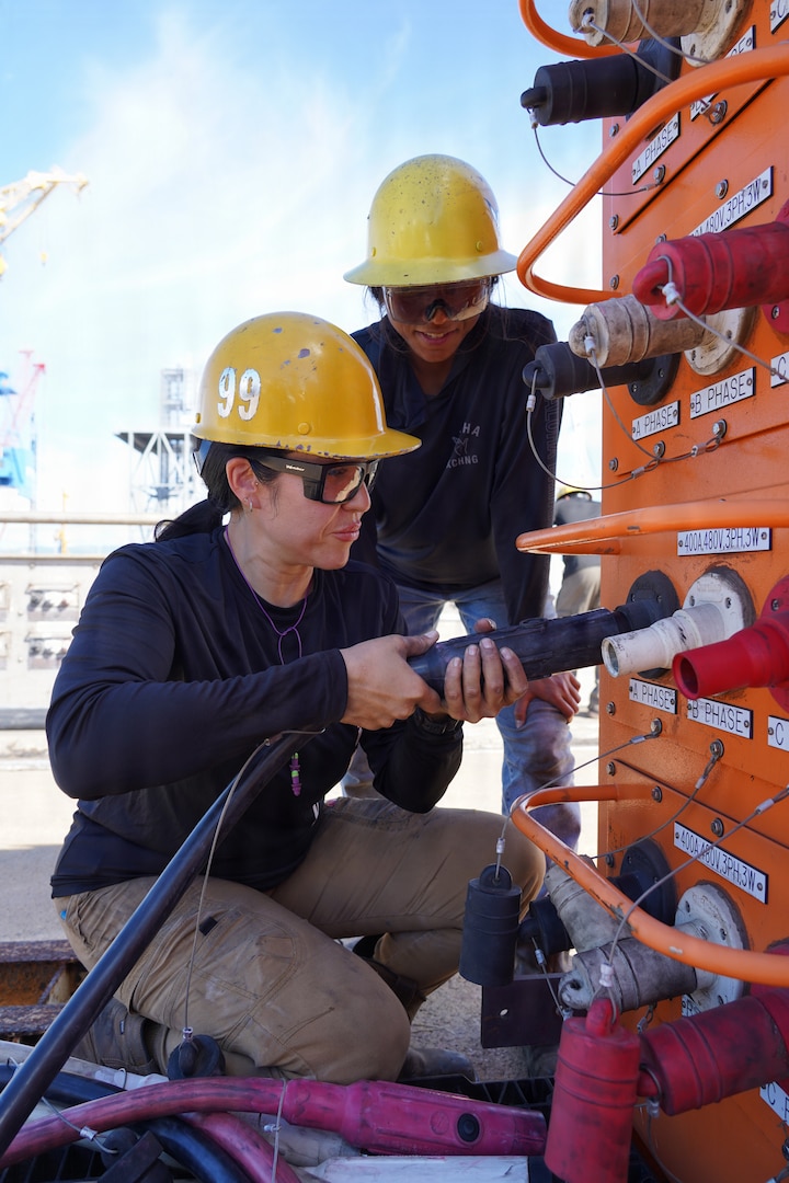 From left, Halau-Lani Davan, electrician, and Danalynne Llacuna, pipefitter, both with Pearl Harbor Naval Shipyard and Intermediate Maintenance Facility (PHNSY & IMF) connect a T500 shore power electrical cable to an electrical load center at Joint Base Pearl Harbor-Hickam, July 7, 2026.