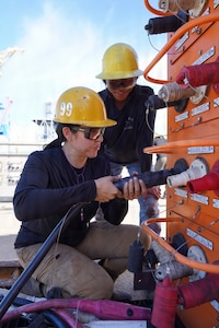 From left, Halau-Lani Davan, electrician, and Danalynne Llacuna, pipefitter, both with Pearl Harbor Naval Shipyard and Intermediate Maintenance Facility (PHNSY & IMF) connect a T500 shore power electrical cable to an electrical load center at Joint Base Pearl Harbor-Hickam, July 7, 2026.