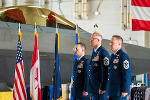U.S. Air Force Lt. Gen. Robert Davis, commander of Alaskan NORAD Region, Alaskan Command and Eleventh Air Force; Chief Master Sgt. Heath Tempel, outgoing senior enlisted leader of ANR, ALCOM, and command chief of 11th AF; and Chief Master Sgt. Kevin Helms, incoming senior enlisted leader of ANR, ALCOM, and command chief of 11th AF, stand at attention on stage during the combined headquarters change-of-responsibility ceremony at Joint Base Elmendorf-Richardson, Alaska, Aug. 11, 2026. The change-of-responsibility ceremony is a time-honored Air Force tradition that recognizes the vital role of the noncommissioned officer corps and marks the formal transfer of senior enlisted leadership. (U.S. Air Force photo by Airman 1st Class Theodore Gowdy)