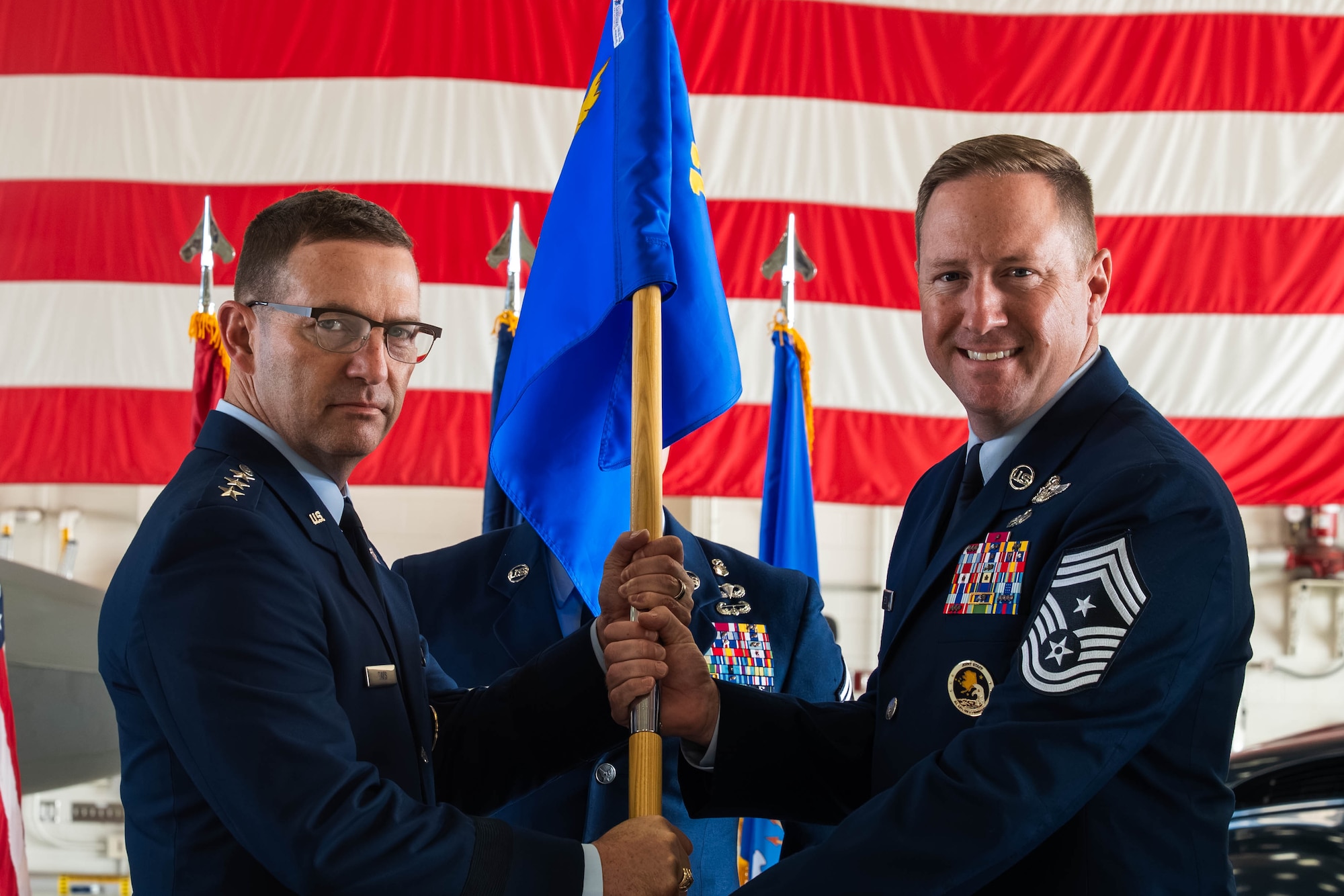 U.S. Air Force Lt. Gen. Robert Davis, commander of ANR, ALCOM and 11th Air Force, entrusts the unit colors to Chief Master Sgt. Kevin Helms, incoming command chief of 11th AF, during a change-of-responsibility ceremony at Joint Base Elmendorf-Richardson, Alaska, Aug. 11, 2026. The transfer of the guidon publicly demonstrates the commander's trust in the incoming chief to advocate for the welfare, readiness and morale of the enlisted force. (U.S. Air Force photo by Airman 1st Class Theodore Gowdy)
