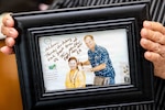 Haru Uchira, U.S. Naval Hospital Okinawa’s (USNHO) barber, holds a framed photo of herself and then-Capt. Terry Moulton, former commanding officer of USNHO from 2009 to 2011, inside the hospital barber shop on Camp Foster, Okinawa, Japan, Aug. 13, 2026. Uchira retired after 56 years of service, witnessing the hospital's operational transition from the U.S. Army to the U.S. Navy in 1977, multiple organizational redesignations, and its relocation from Camp Lester to Camp Foster in 2013. (U.S. Navy photo by Mass Communication Specialist 1st Class Simon Pike)