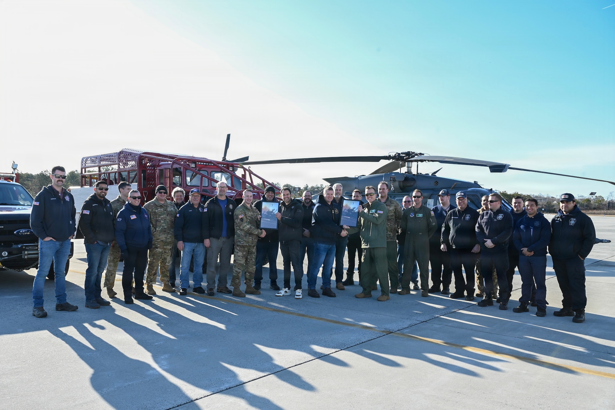 Southampton Fire Department First Assistant Chief Ricky Fowler (right) and Capt. Jason Poremba (Left) present representatives of the New York Air Guard’s 106th Rescue Wing and Army Guard’s 3rd Battalion, 142nd Assault Helicopter Battalion with a framed photograph at Francis S. Gabreski Air National Guard Base in Westhampton Beach, N.Y., January 9, 2026.  The image, presented as a token of appreciation for the Guard’s critical support during a wildfire on March 8, 2025, shows a New York Army National Guard UH-60M Black Hawk releasing water from a "Bambi Bucket" directly over a Southampton brush truck on the front lines. (U.S. Air National Guard photo by Tech. Sgt. Daniel H. Farrell)
