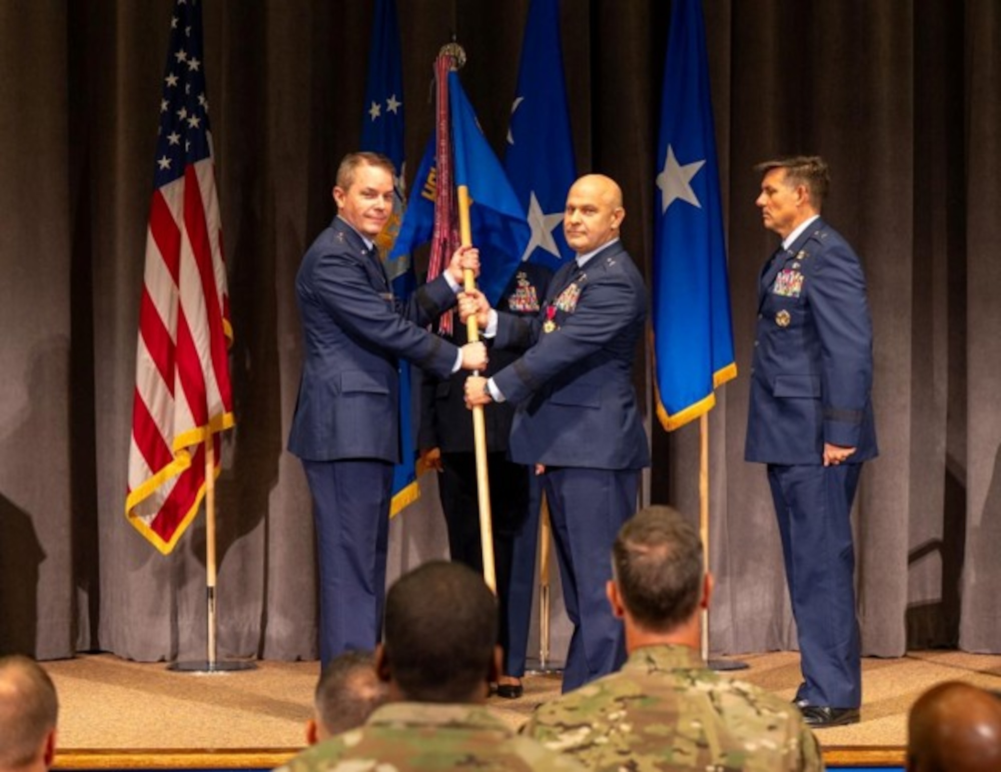U.S. Air Force Brig. Gen. Joseph Sheffield, Jeanne M. Holm Center outgoing commander, passes the Holm Center guidon to Maj. Gen. Jeffrey W. Nelson, Air Force Accessions Center commander, during a change of command ceremony at Officer Training School, Maxwell Air Force Base, Alabama, Aug. 18, 2026. The Holm Center is responsible for producing approximately 85% of officers entering the Department of the Air Force total force, making its mission critical to developing and preparing the next generation of Airmen and Guardians. (U.S. Air Force photo by Senior Airman Tanner Doerr)