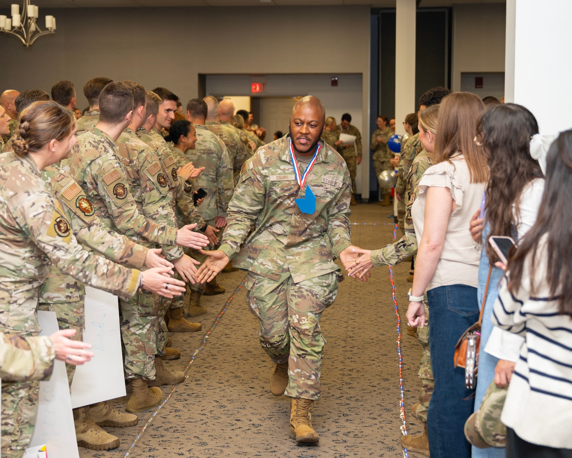 A man in camouflage uniform runs between two groups of people slapping hands in 'low-five' manner.