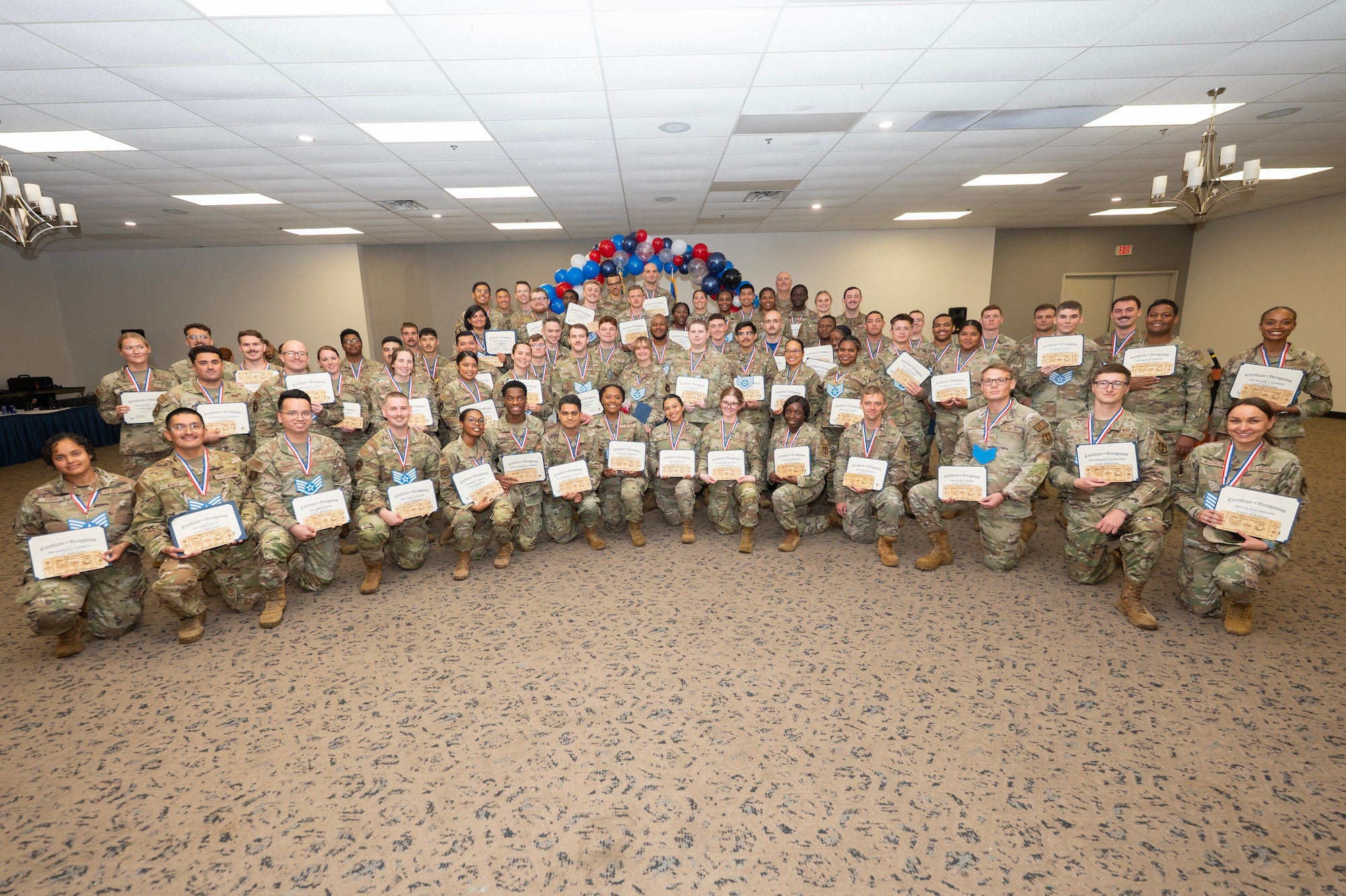 A large group of people in camouflage uniforms pose holding certificates.