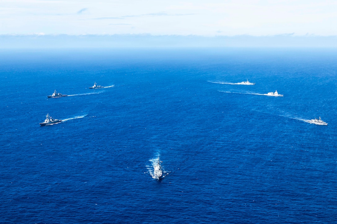 Two sets of three ships sail in opposite directions as another ship leads the way in blue waters during the day.