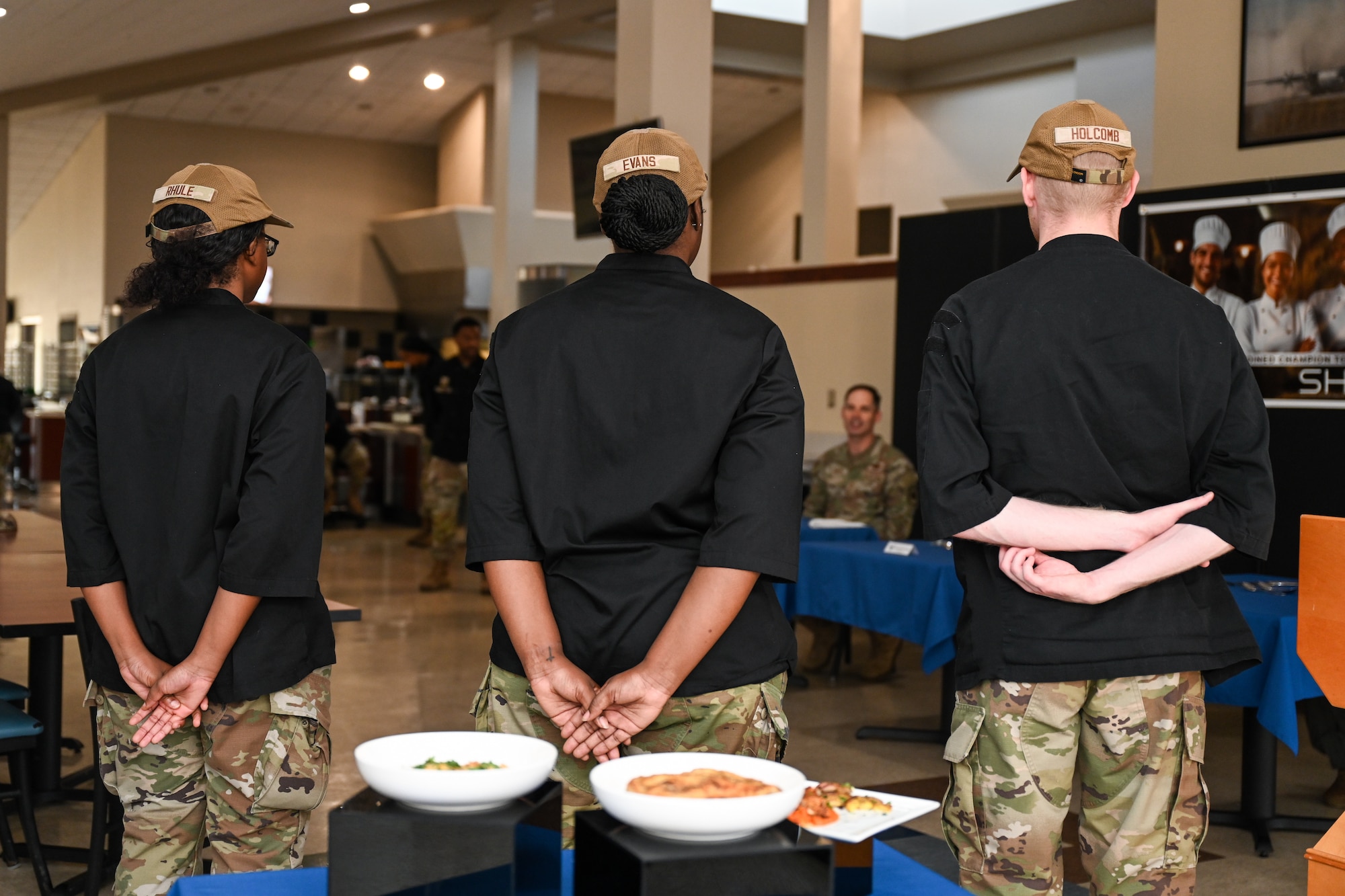 Airmen stand in front of food that they made.