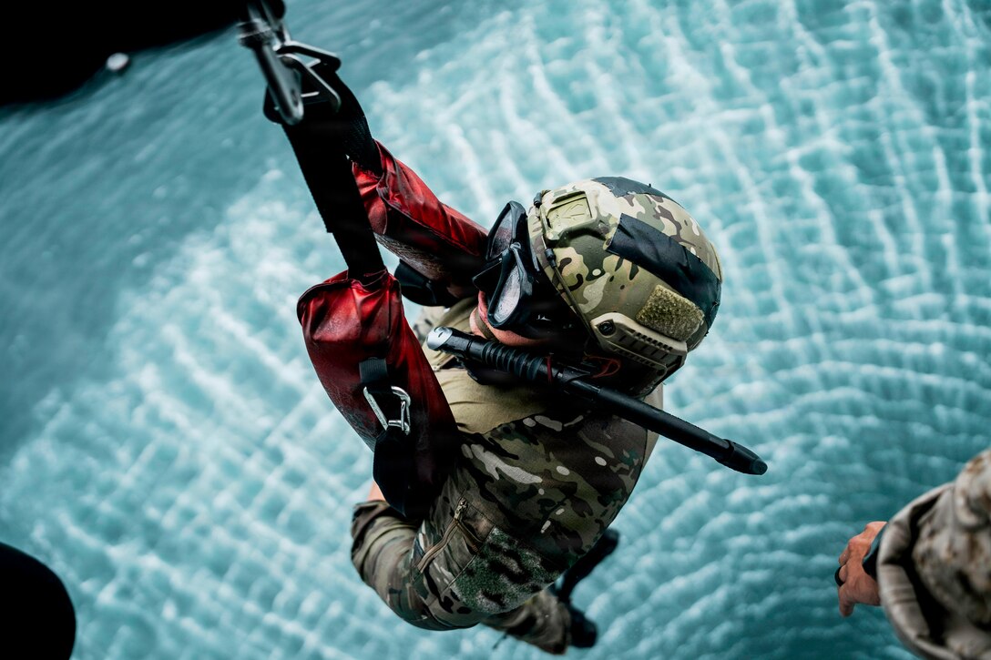 A sailor wearing goggles and a helmet holds onto a rope over choppy blue water.