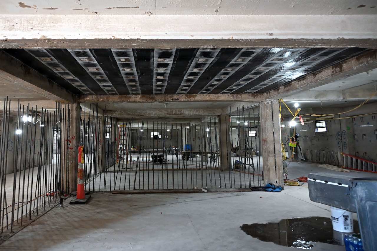 The inside of a building under construction. A man in construction safety gear is in the background.
