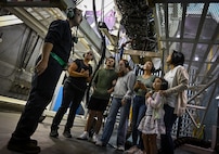 A group of people stand beneath a F-15E Strike Eagle engine in a test cell.