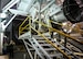 A maintenance Airman gestures for a tour group to move forward in a engine test cell.