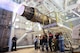 A group of people stand beneath a F15-E Strike Eagle Egine running at full afterburner in a test cell.