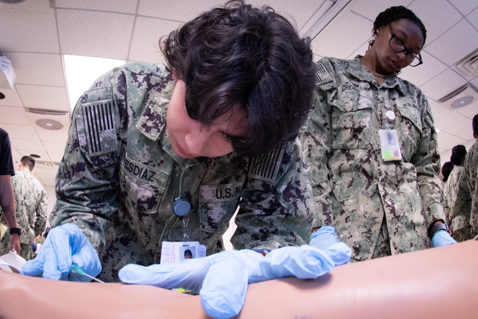 *Training* Hospitalman Rosemary Nieves Diaz, center, trains to insert an IV needle in a training aid as Hospitalman Jamiyah Crider, right, looks on during a skills fair conducted Thursday, August 20, 2026, at Navy Medicine Readiness and Training Command Cherry Point.  The Skills Fair evaluated the knowledge of corpsmen assigned to the facility and trained them on competencies and tasks expected of them in an operational environment.