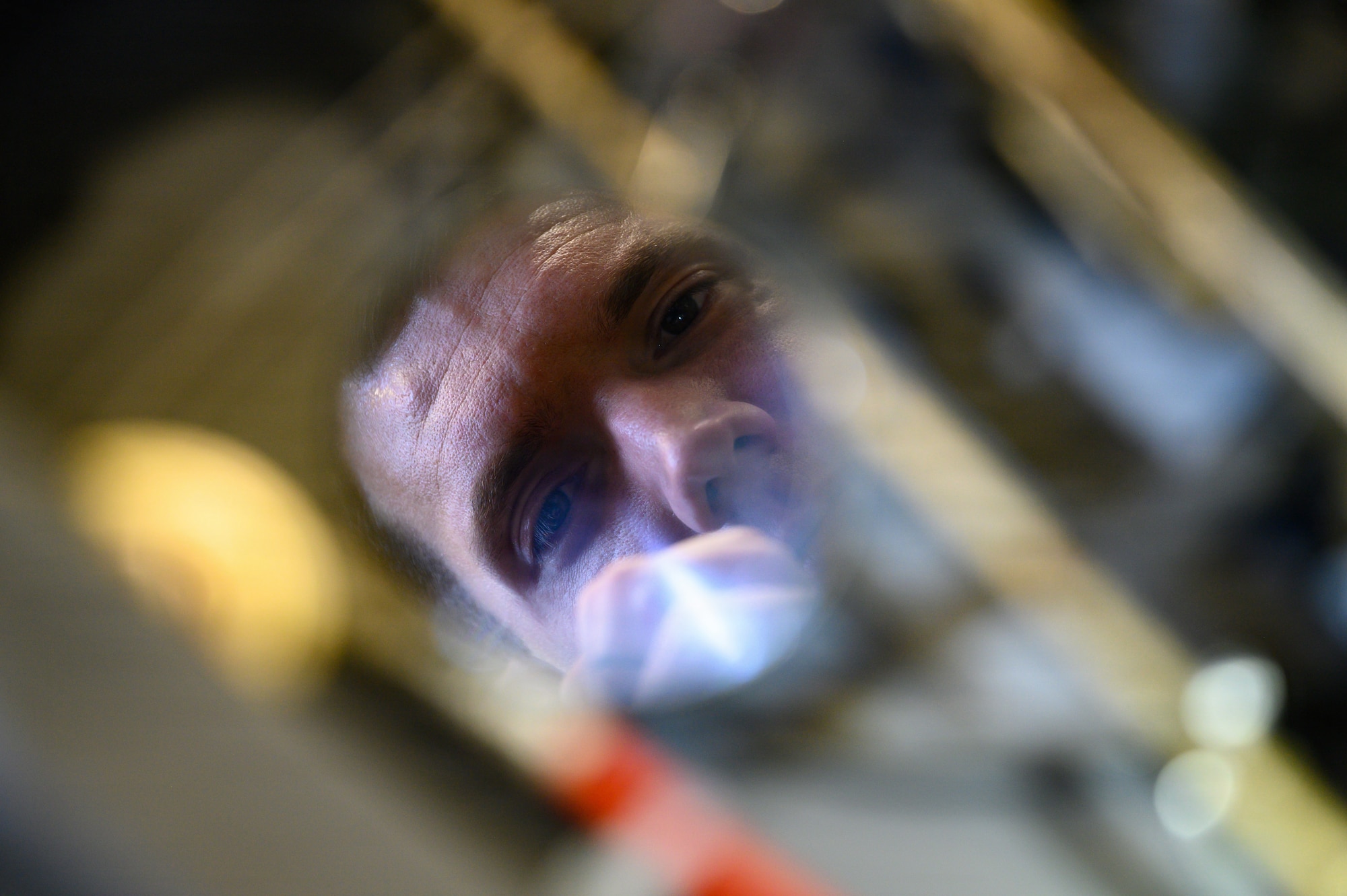 A man inspects an ejection seat with a mirror.