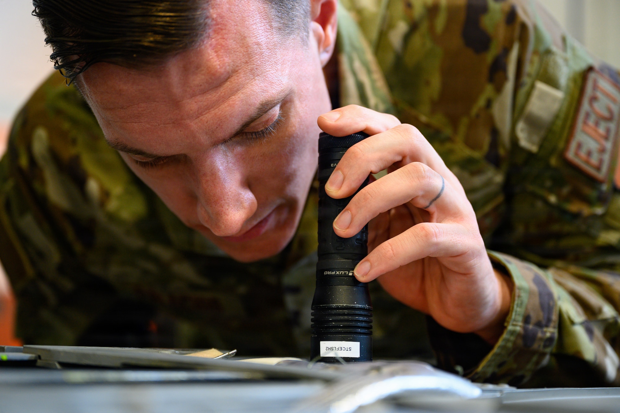 A man looks at an ejection seat with a flashlight.