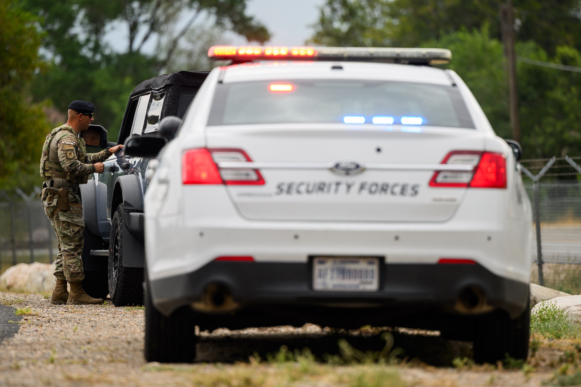 75th Security Forces patrol vehicle positioned along a roadway during a speed enforcement operation. A patrolman can be seen in the background talking to a pulled over motorist through their window.