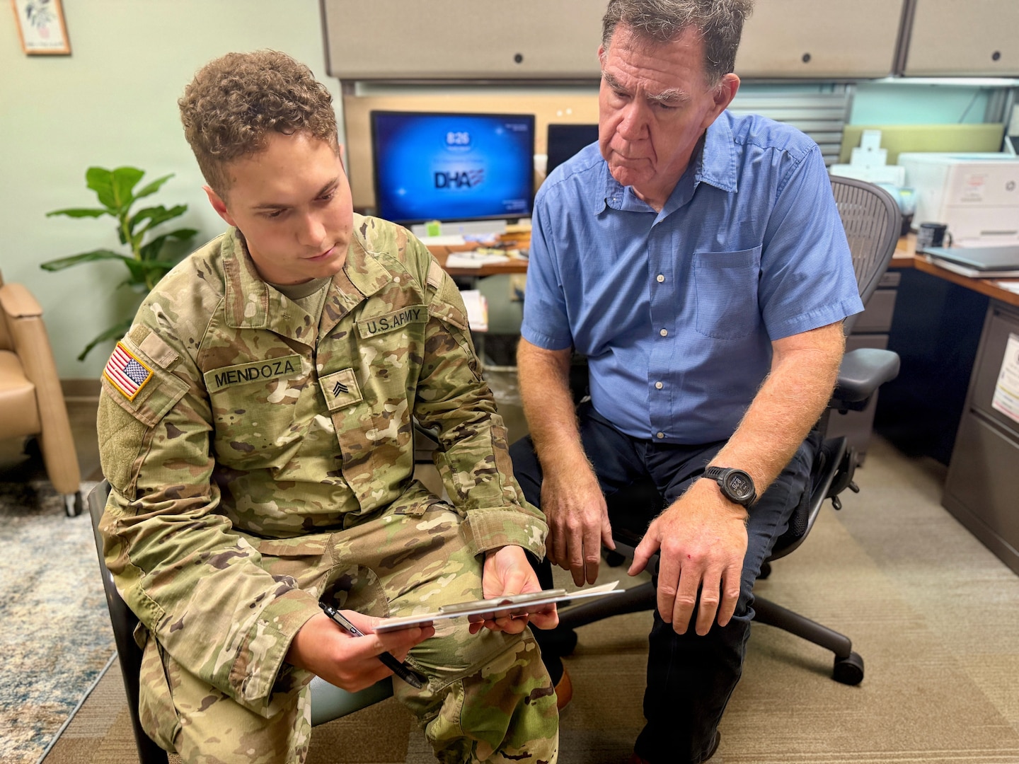 Mental health provider in a clinical setting looks over a chart as a patient looks on.