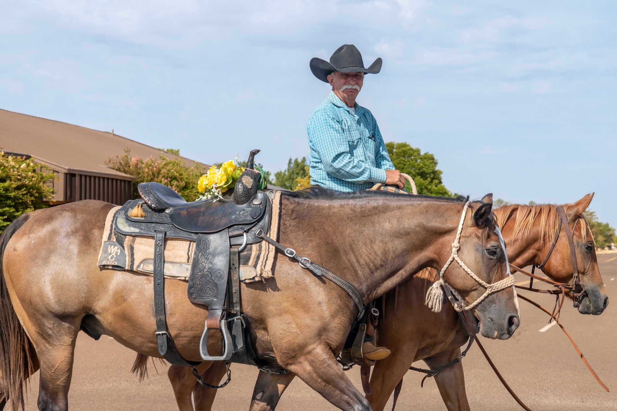 Randy Braker, local rancher, rides alongside the late Gary ‘Bull’ Watkins horse, affixed with yellow roses on the saddle to honor him during the 28th Annual Cattle Drive at Altus Air Force Base, Oklahoma, Aug. 20, 2026. Watkins provided the horses and saddles for the command team and additional commanders for many years. (U.S. Air Force photo by Senior Airman Kari Degraffenreed)