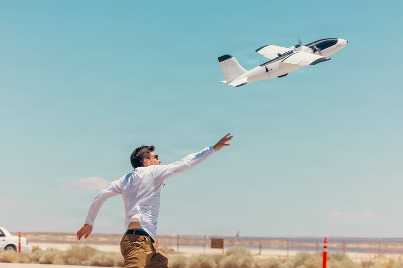 A man reaches up as a drone flies into the sky.