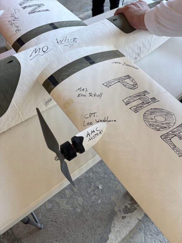 A person holds a white military drone with writing on it.