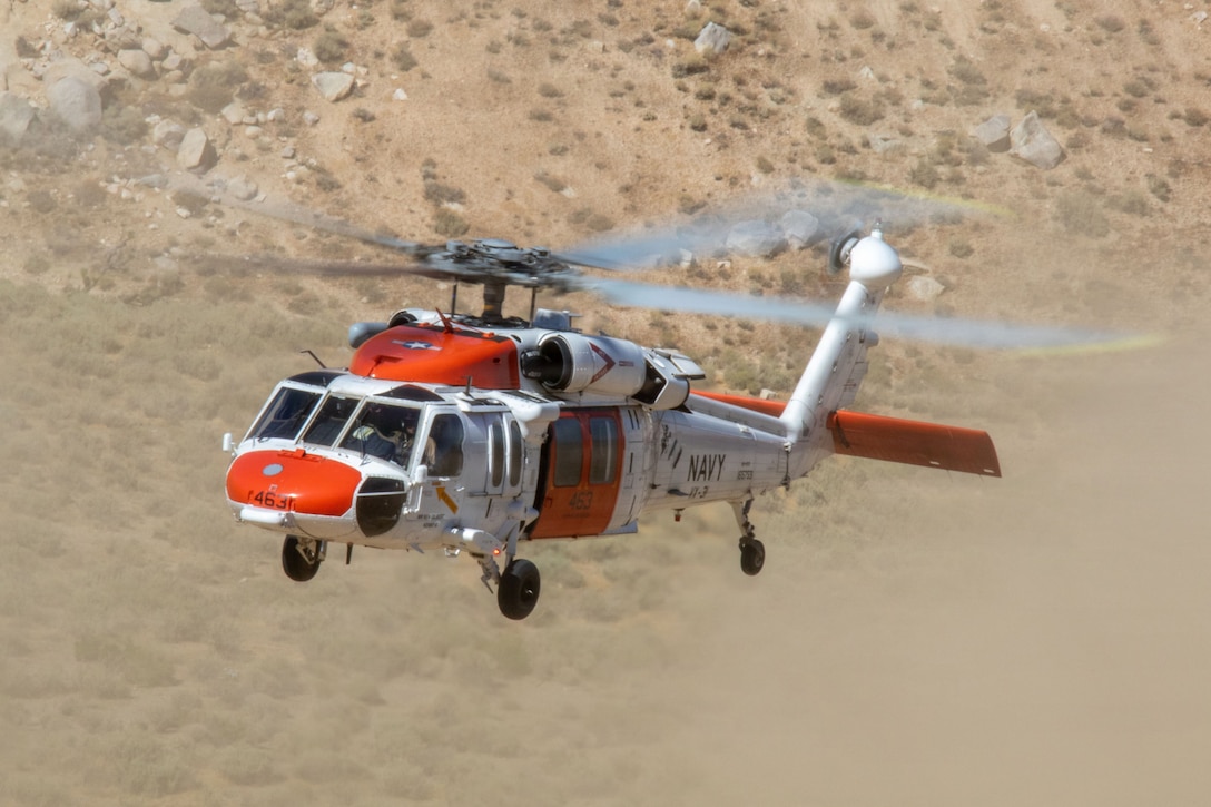 A helicopter flies over a desert environment.