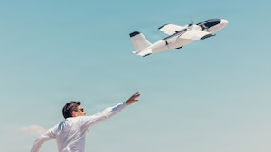 A person reaches up as a drone flies into the sky.
