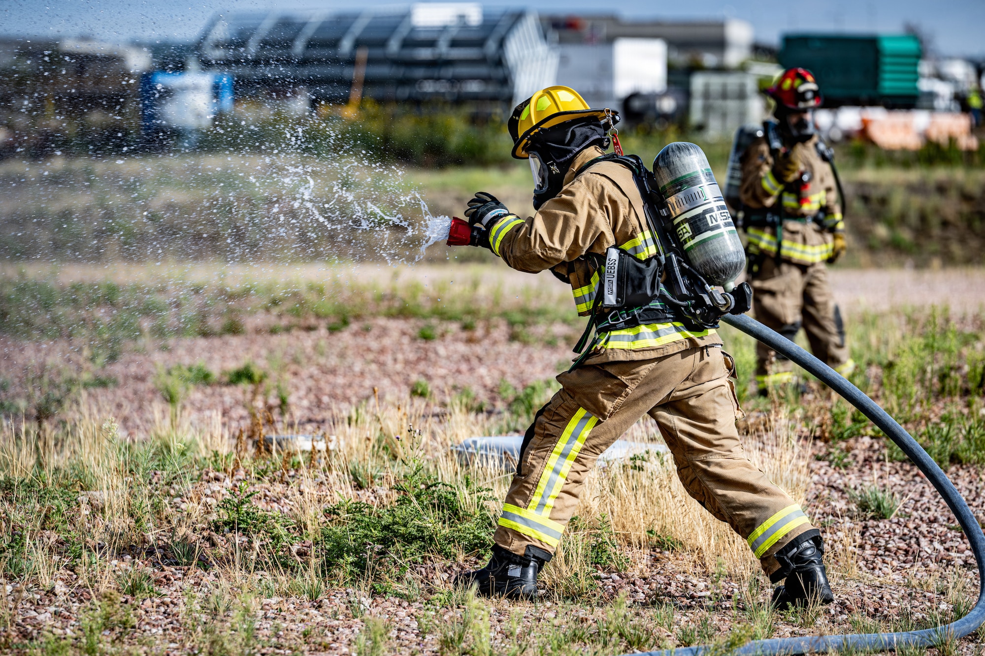 A firefighter assigned to the 21st Civil Engineer Squadron conducts fire suppression operations during a full-scale emergency response exercise