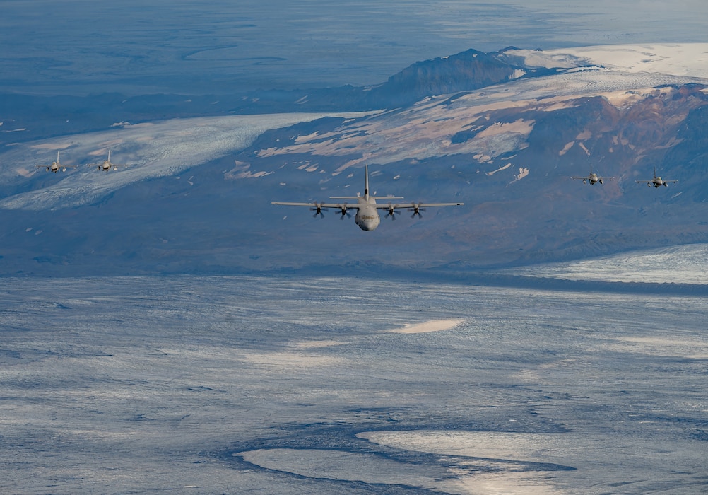 Four Belgian Air Force F-16 Fighting Falcon aircraft fly in formation with a U.S. Air Force C-130J Super Hercules aircraft assigned to the 37th Airlift Squadron above glacier-covered terrain in Iceland during exercise Northern Viking 26