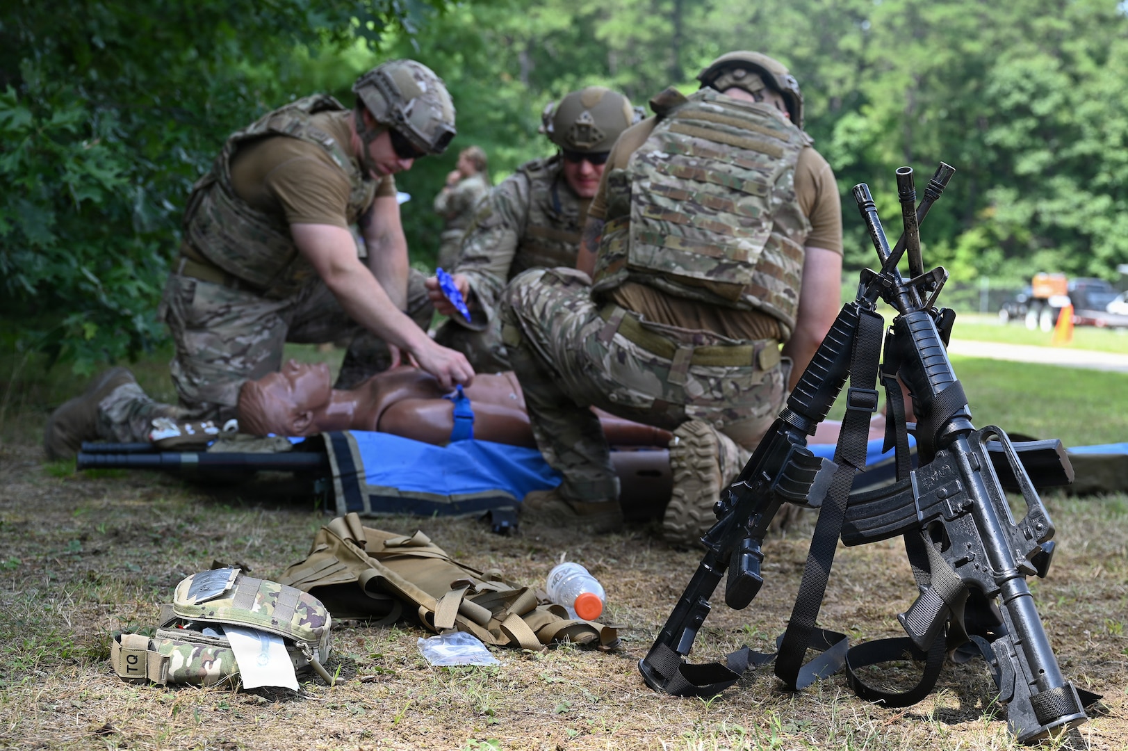 Weapons rest in a stack as explosive ordnance disposal Airmen provide Tactical Combat Casualty Care to a simulated patient at Barnes Air National Guard Base, Westfield, Mass., Aug. 20.