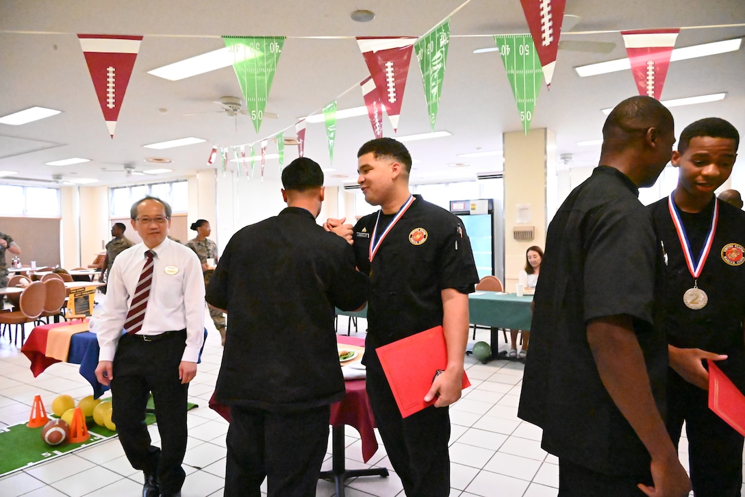 (Center) Corporal Eli Lancelot celebrates winning first place at the Marine Corps Installations Pacific Food Services Specialist of the Quarter competition at Combined Arms Training Center, Camp Fuji, August 19, 2026. (U.S. Marine Corps photo by Song Jordan)