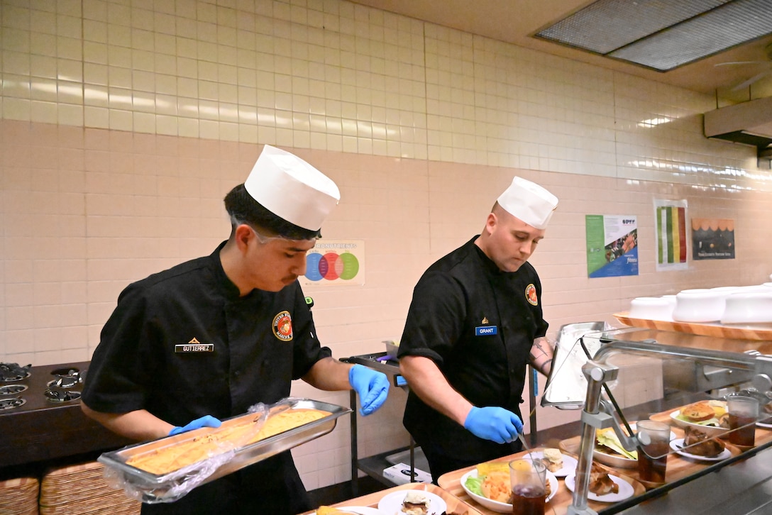 (Right to Left) Lance Corporal Eric Gutierrez and Corporal William Grant, assigned to Combined Arms Training Center, Camp Fuji finesse their meals for the judges during the Marine Corps Installations Pacific Food Services Specialist of the Quarter at Camp Fuji, August 19, 2026. (U.S. Marine Corps photo by Song Jordan)