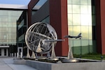 A metal sculpture that includes a globe with the words "U.S. Strategic Command" on it sits outside a building.