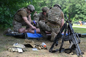 Weapons rest in a stack as explosive ordnance disposal Airmen provide Tactical Combat Casualty Care to a simulated patient at Barnes Air National Guard Base, Westfield, Mass., Aug. 20.
