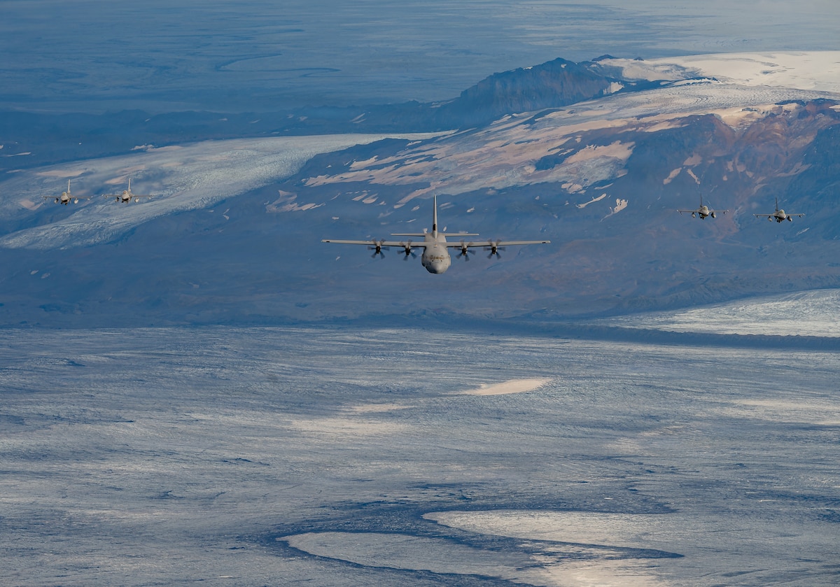Four Belgian Air Force F-16 Fighting Falcon aircraft fly in formation with a U.S. Air Force C-130J Super Hercules aircraft assigned to the 37th Airlift Squadron above glacier-covered terrain in Iceland during exercise Northern Viking 26