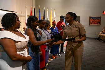 Presiding Officer Lt. Erica Weatherford assigned to Navy Medicine Readiness and Training Command (NMRTC) Bethesda, hands out appreciation certificates to the family of Chief Hospital Corpsman Avesta El during her retirement ceremony at Walter Reed National Military Medical Center on August 14, 2026. NMRTC Bethesda mission is to maximize warfighter performance through optimized medical readiness tailored to operational requirements; enhance the readiness of the medical force to sustain expeditionary medical capability; and train and develop the Navy Medicine Force. (U.S. Navy photo Mass Communication Specialist Second Class Alec Kramer)