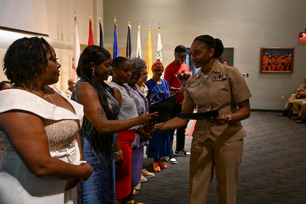 Presiding Officer Lt. Erica Weatherford assigned to Navy Medicine Readiness and Training Command (NMRTC) Bethesda, hands out appreciation certificates to the family of Chief Hospital Corpsman Avesta El during her retirement ceremony at Walter Reed National Military Medical Center on August 14, 2026. NMRTC Bethesda mission is to maximize warfighter performance through optimized medical readiness tailored to operational requirements; enhance the readiness of the medical force to sustain expeditionary medical capability; and train and develop the Navy Medicine Force. (U.S. Navy photo Mass Communication Specialist Second Class Alec Kramer)
