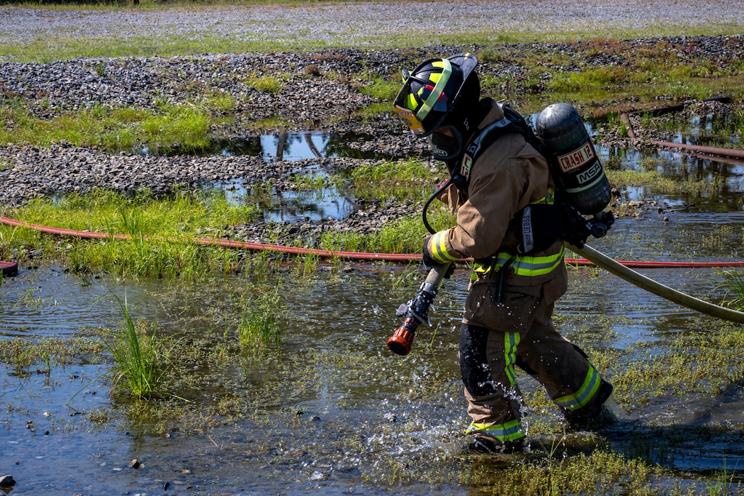 firefighter carries a fire hose through water