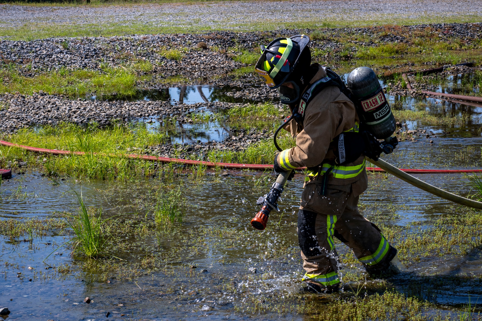 firefighter carries a fire hose through water