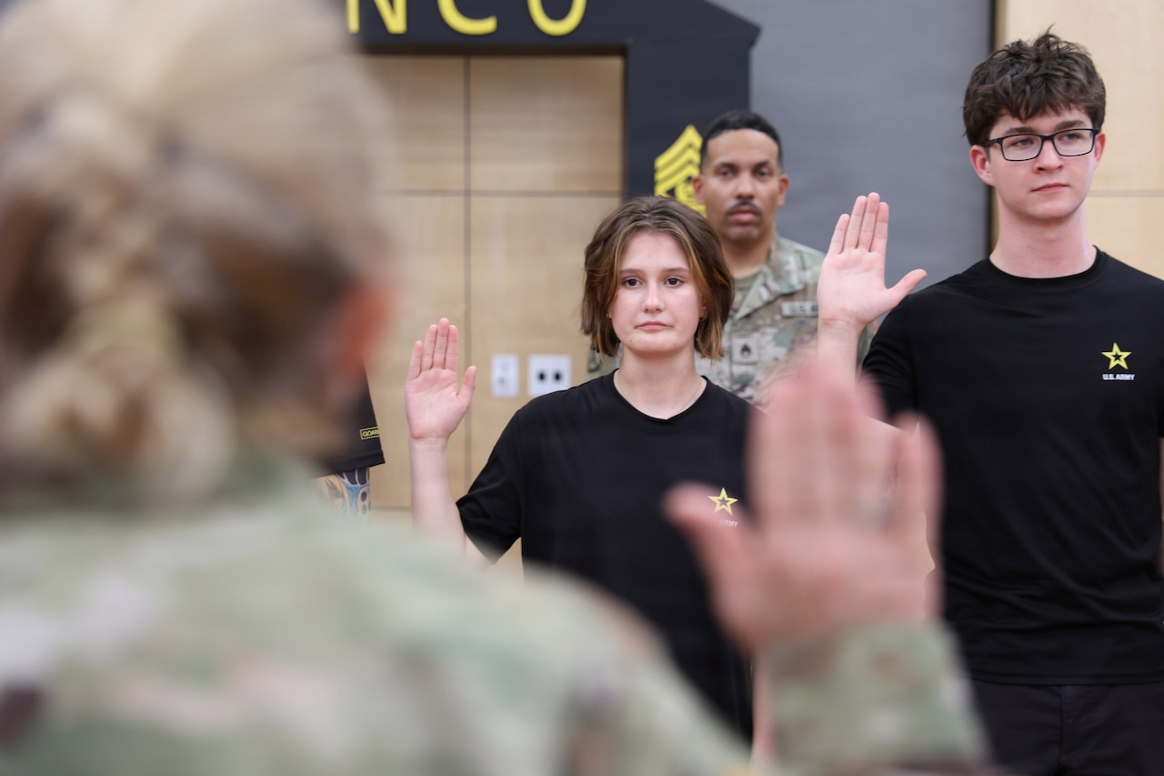 Two people in casual attire hold up their right hands. A person in the foreground in a camouflage military uniform also holds up their right hand.