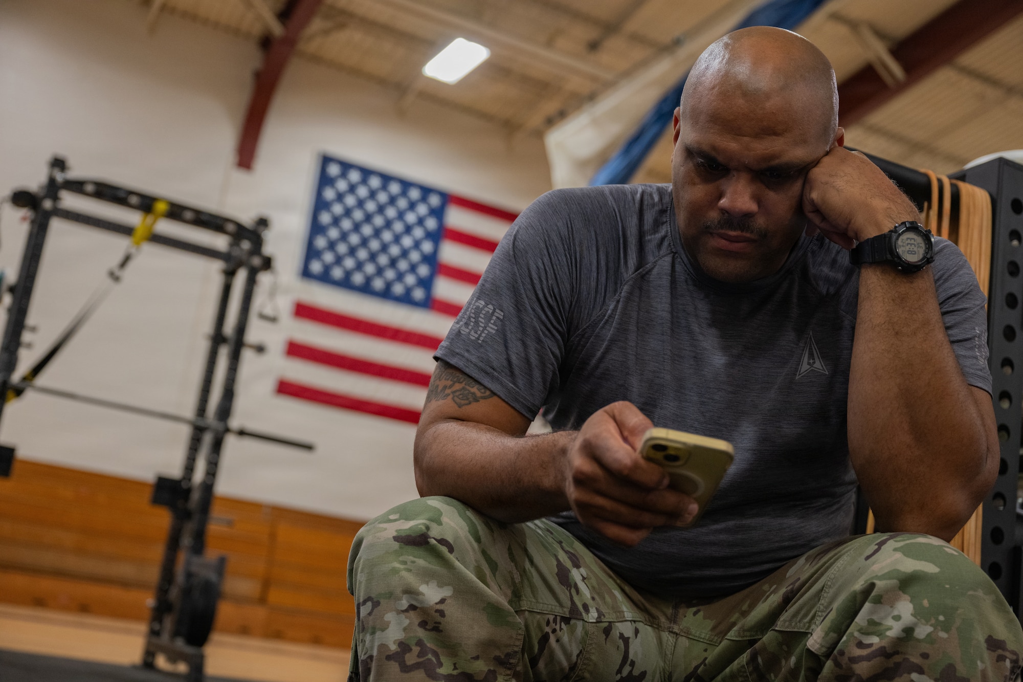 A servicemember looks at their phone during a cognitive challenge in a gym.