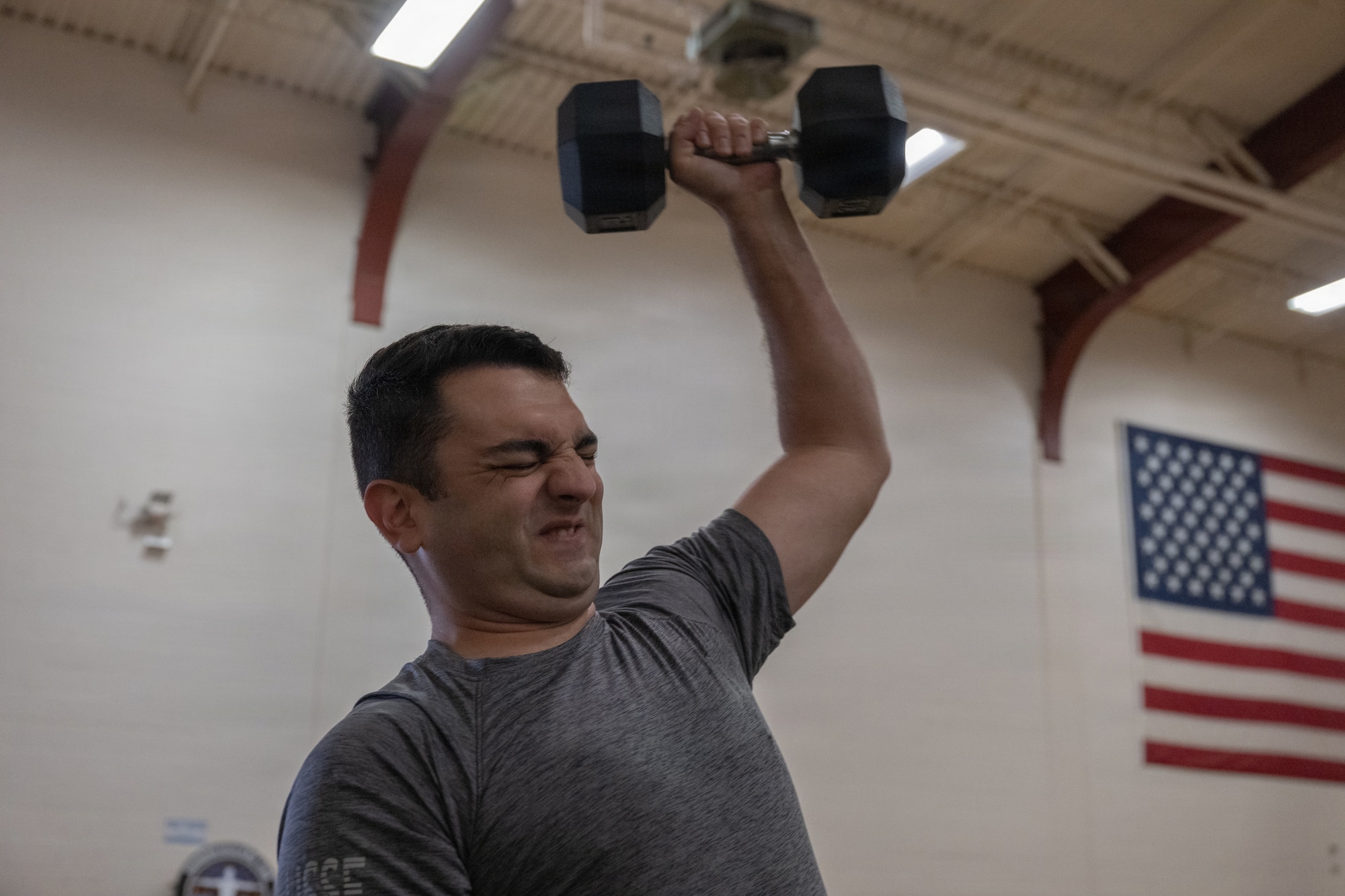 A servicemember lifts a weight over their shoulder in a gym.